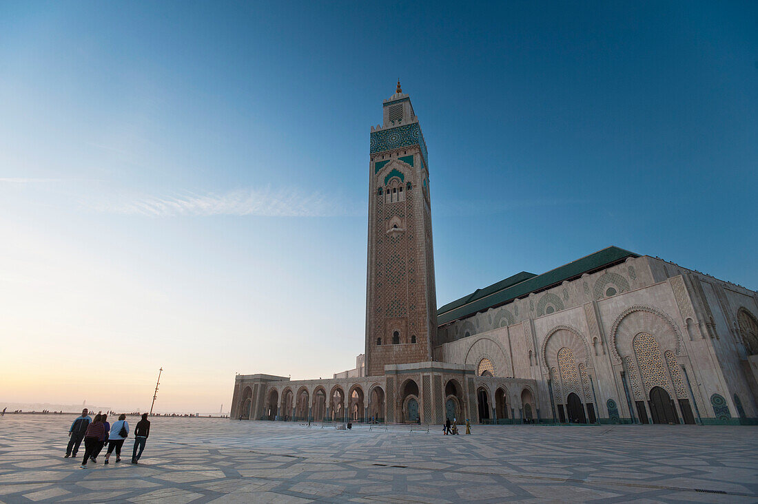 Morocco,People walking across courtyard in front of Hassan II mosque at dusk,Casablanca