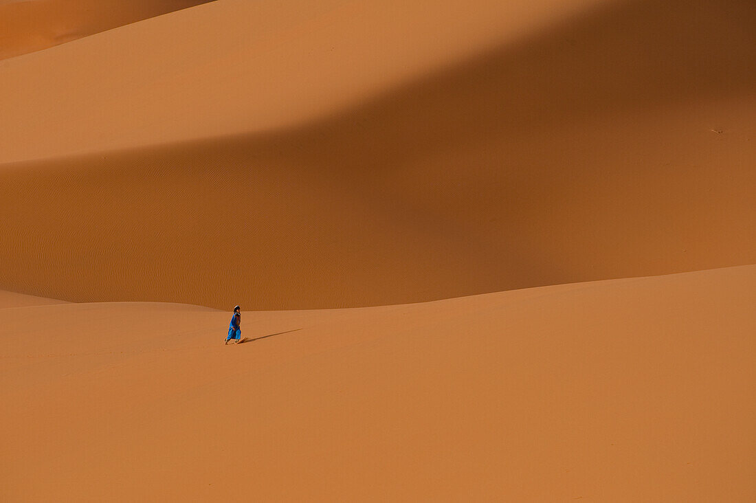 Morocco,Berber 'Blue man' walking across sand dunes in Erg Chebbi area,Sahara Desert near Merzouga