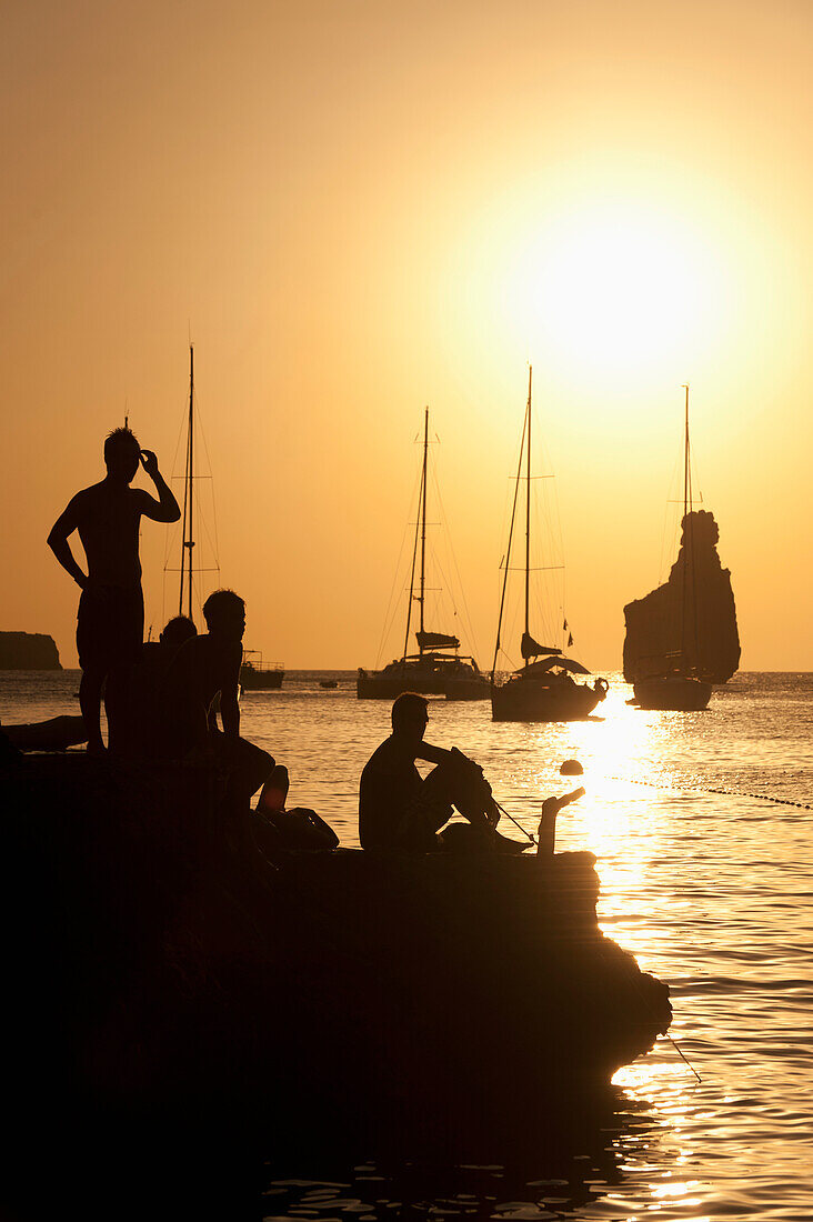 Spain,People watching sunset on rocks beside Benirras beach,Ibiza