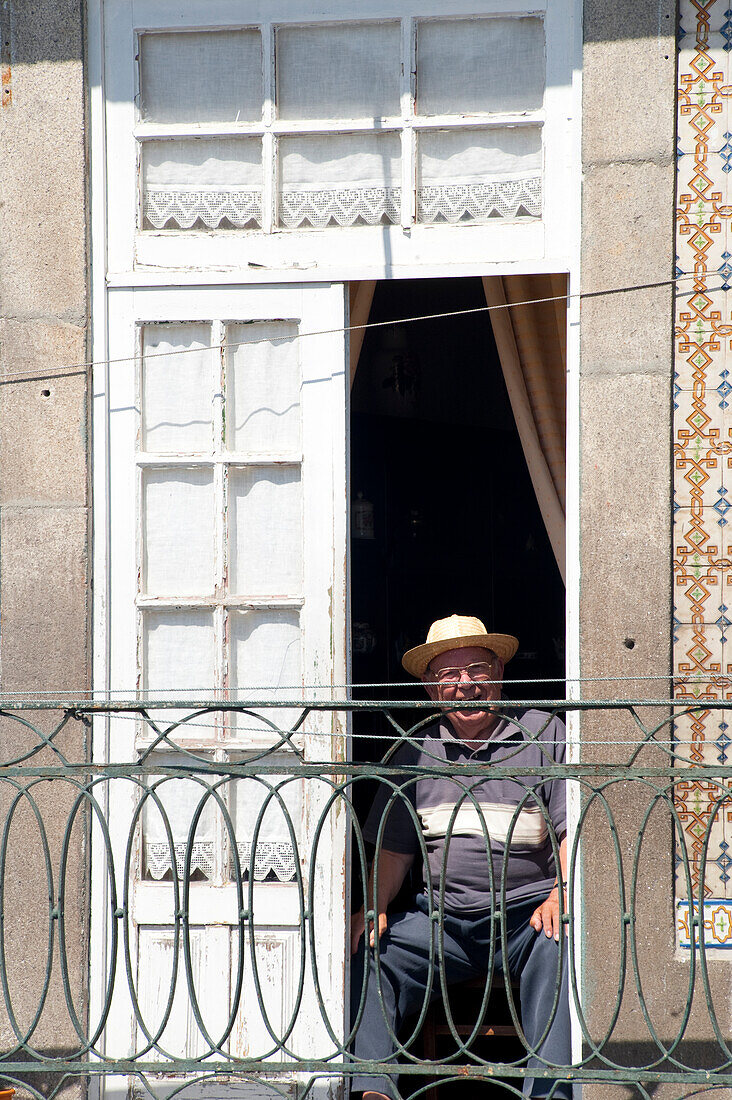 Alter Mann sitzt auf einem Balkon in Ribeira, Porto, Portugal