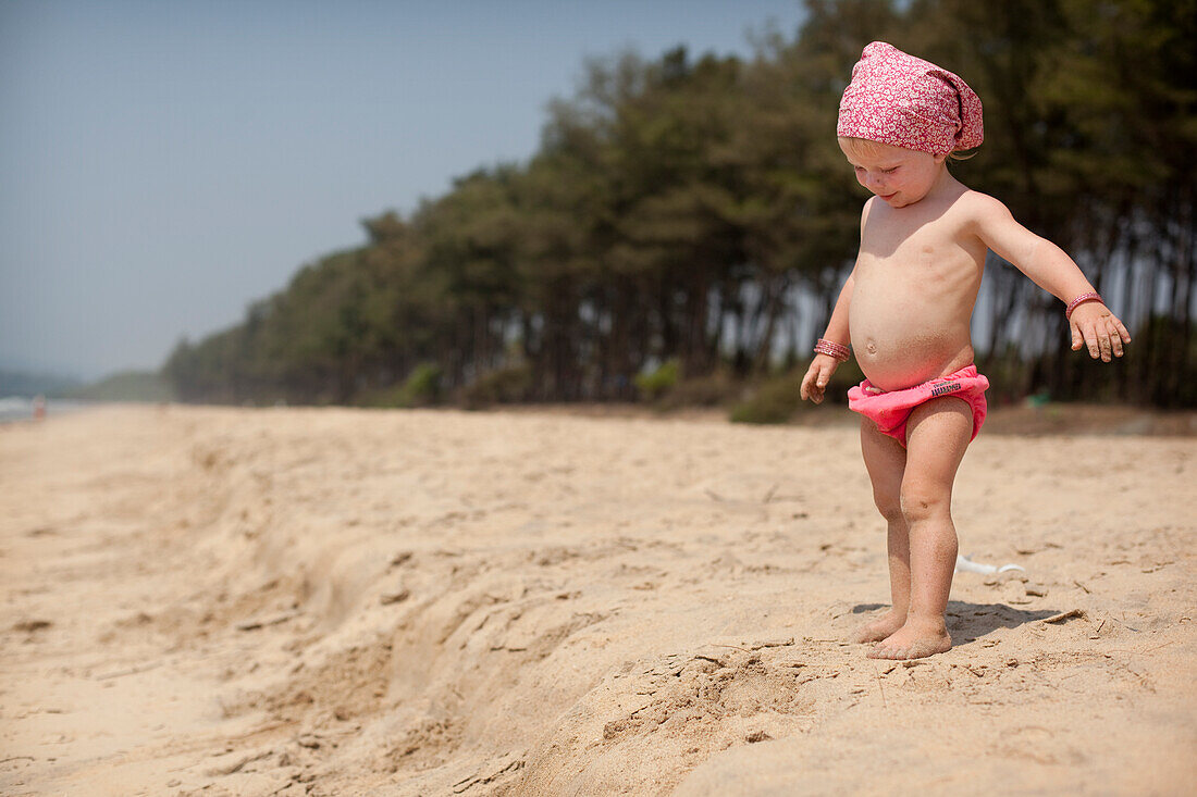 A toddler wearing waterproof nappy pants,plays on Turtle Beach,Goa,India.