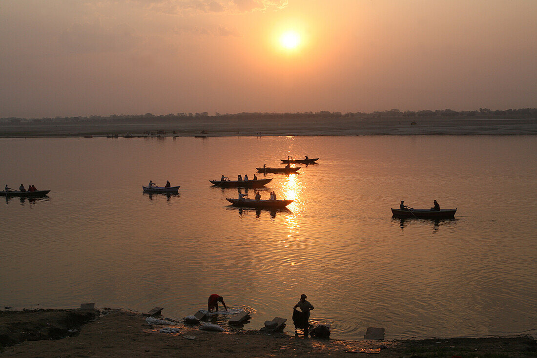 Boote auf dem Ganges und Wäsche, die bei Sonnenaufgang gewaschen wird. Die Kultur von Varanasi ist eng mit dem Ganges und der religiösen Bedeutung des Flusses verbunden: Sie ist die "religiöse Hauptstadt Indiens" und ein wichtiges Pilgerziel.