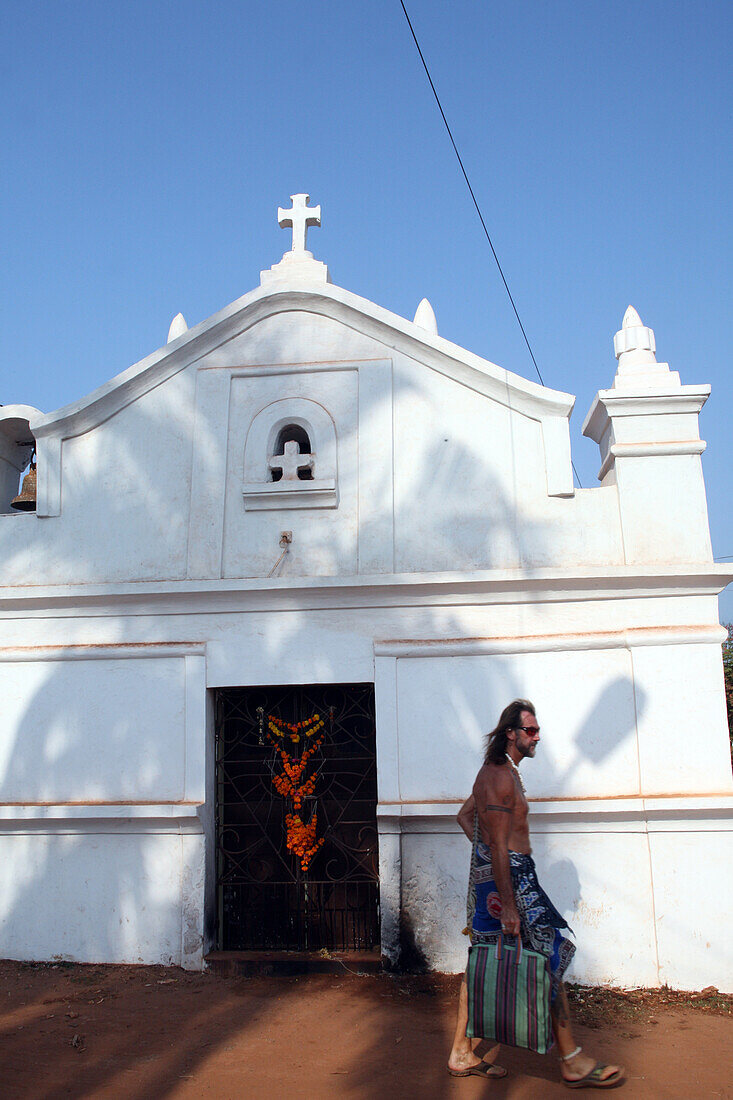 Ein Mann geht an einer Kirche vorbei, das Christentum ist die Volksreligion in der ehemaligen portugiesischen Kolonie Goa, und macht sich auf den Weg zum weltberühmten Anjuna-Flohmarkt, der mittwochs am Anjuna Beach stattfindet, im Bundesstaat Goa, Indien, Asien.