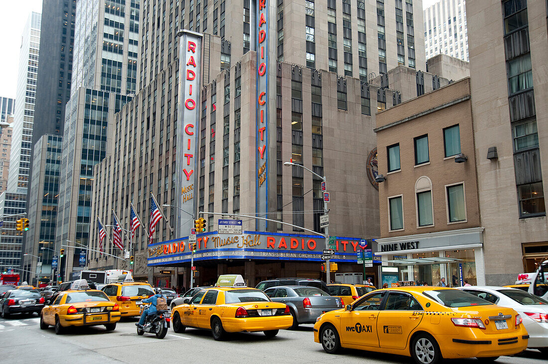 Taxis im Vorbeifahren an der Radio City Music Hall, dem berühmten Unterhaltungszentrum im Rockefeller Center, Midtown Manhattan, New York, USA