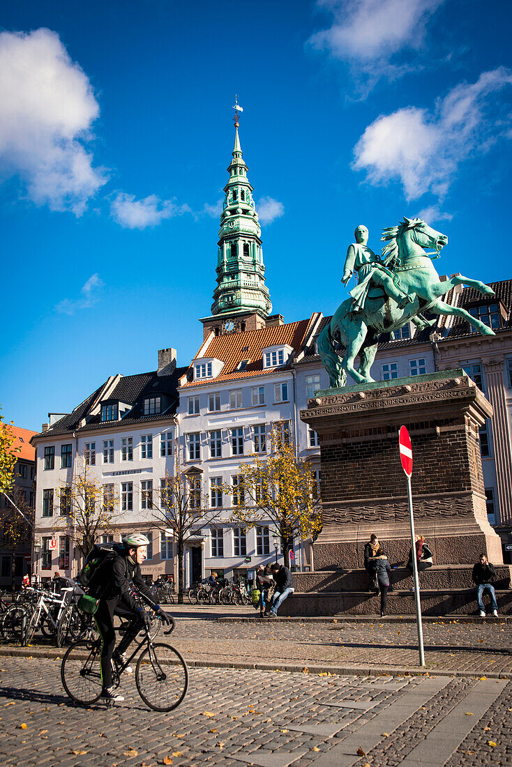 Denmark,Cyclist passing in front of Bishop Absalon equestrian statue in Hojbro Plads and views of Nikolaj on background,Copenhagen