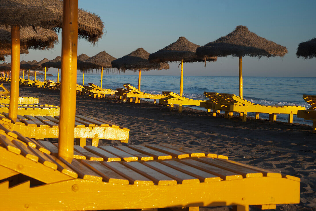 Spain,Yellow beach chairs and straw sun umbrellas,Malaga