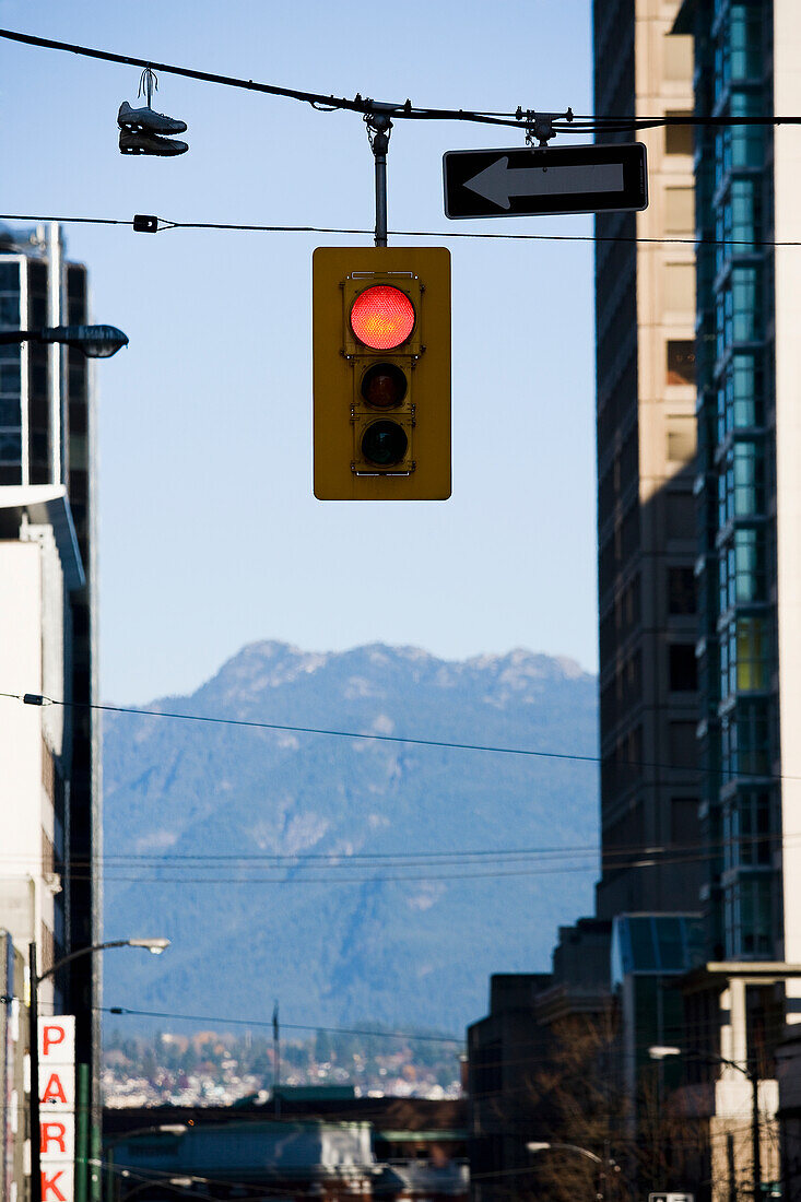 Ampel, die an einem Kabel zwischen Gebäuden aufgehängt ist, mit Blick auf einen Berg im Hintergrund, Vancouver, British Columbia, Kanada