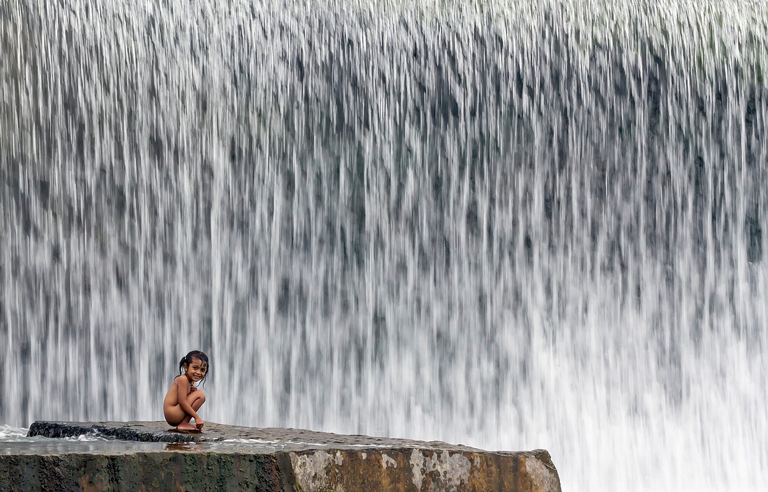 Indonesia,Bali,who were eventually responsible for building this weir,Klungkung,Klungkung was last kingdom in Bali to hold out against Dutch colinisers,Girl crouching on rock close to weir near Kerta Gosa Temple