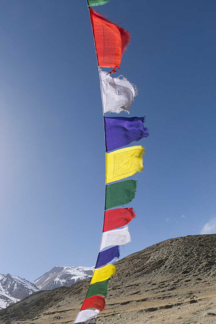 Bunte Gebetsfahnen vor blauem Himmel mit Gipfeln in der Ferne, Oberes Mustang-Tal, Nepal