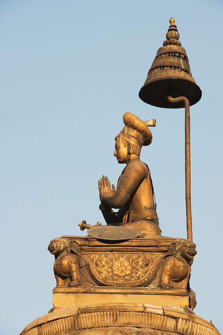 Eine vergoldete Statue von König Bhupatindra Malla auf einer Säule mit gefalteten Händen in Gebetshaltung, gefalteten Beinen und einer Schlange, die die Hauptstadt stützt, vor dem Goldenen Tor am Durbar Square, Bhaktapur, Nepal