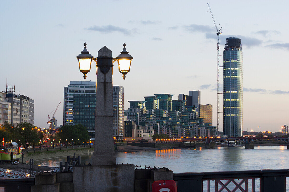 Lamp Post Illuminated At Dusk And Buildings Along The Waterfront,London,England