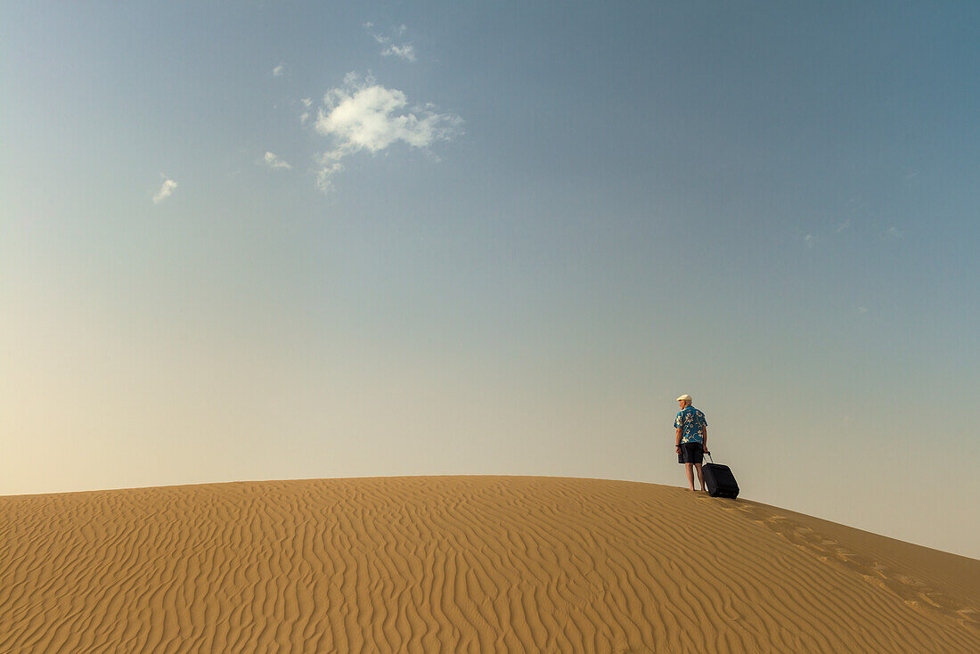 Barfüßiger Mann mit Koffer auf Sanddüne,Dubai,Vereinigte Arabische Emirate
