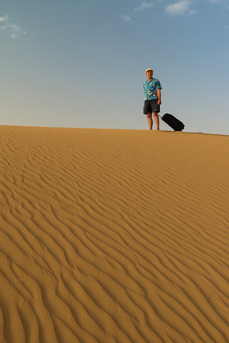 Barfüßiger Mann mit Koffer auf Sanddüne,Dubai,Vereinigte Arabische Emirate