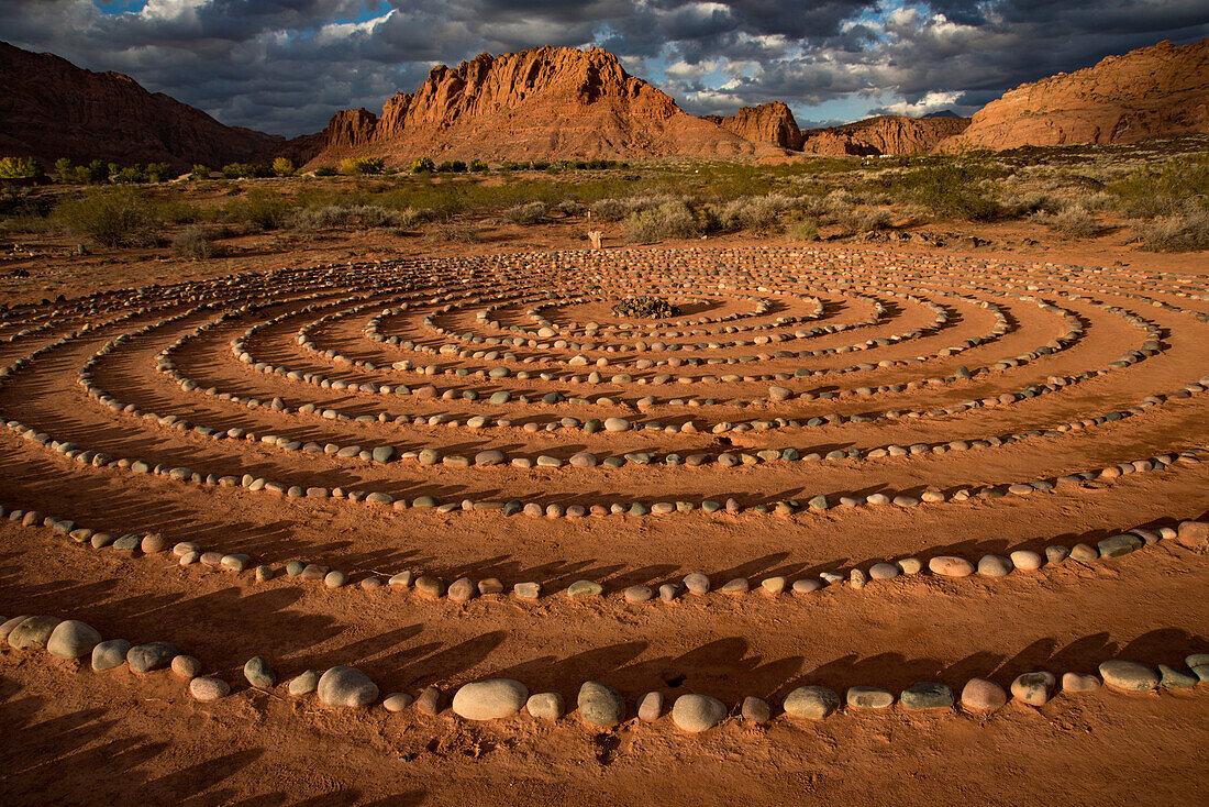 Hiking trail through Snow Canyon,with circles of stones in a meeting area behind the Red Mountain Spa,with meditation maze and Snow Canyon Mountain Range in the background. Red Cliffs Desert Reserve around St George Town with rock cliffs and dark clouds in a blue sky,St George,Utah,United States of America