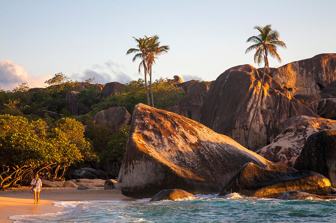 Frau, die am berühmten Strand von The Baths vor den großen, vulkanischen Felsformationen auf den BVI in der Dämmerung spazieren geht, Virgin Gorda, Britische Jungferninseln, Karibik