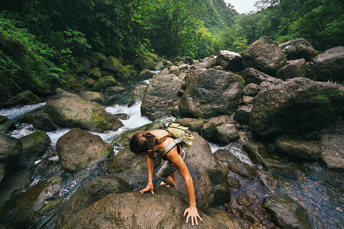 Overhead view of a woman climbing over the slippery,wet rocks along the rushing stream at Trafalgar Falls on the Caribbean Island of Dominica in Morne Trois Pitons National Park,Dominica,Caribbean
