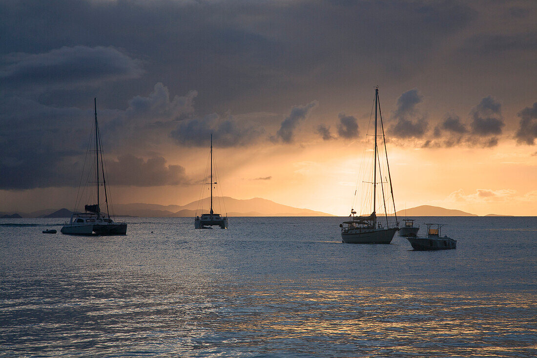 Silhouette of boats moored off shore along the ocean front in Cane Garden Bay against the grey,cloudy sky with golden light at twilight,Tortola,British Virgin Islands,Caribbean