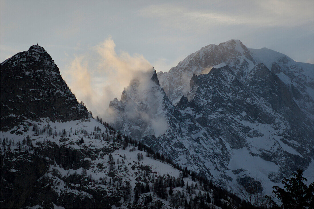 Mont Blanc as seen from Aiguille du Midi,with rugged mountain peaks and clouds backlit by sunlight,Chamonix,France