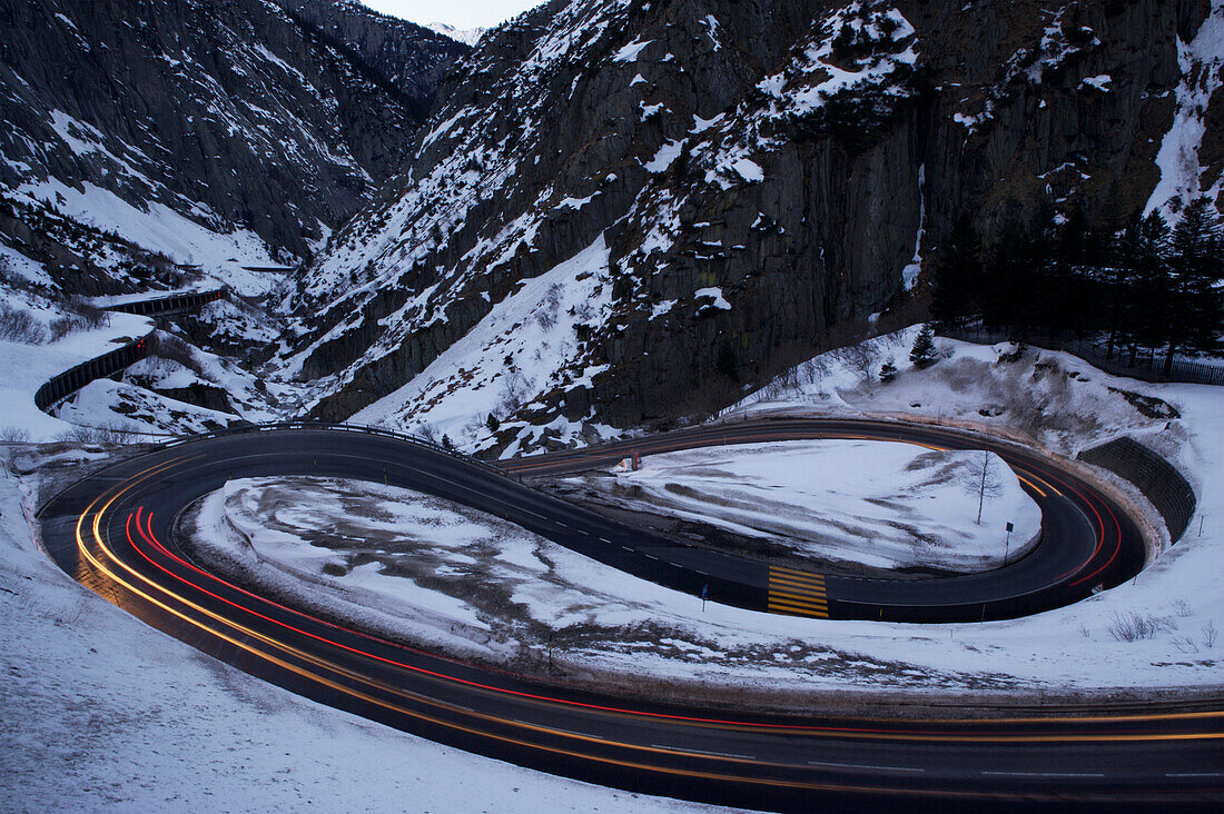 Autolichter verschwimmen auf einer Serpentinenstraße oberhalb des San Gotthard-Tunnels in der Schweiz, Andermatt, Schweiz