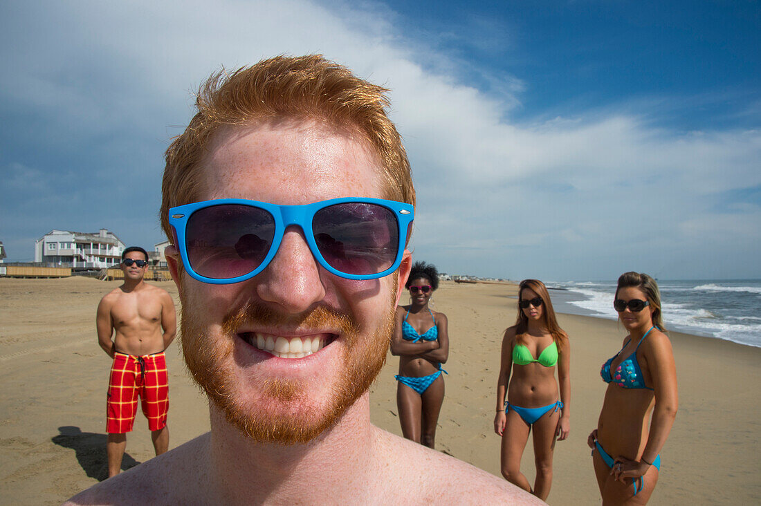 Group of friends in swimwear on Virginia Beach,with a young man in the foreground with a big smile and wearing blue framed sunglasses,First Landing State Park,Virginia,USA,Virginia Beach,Virginia,United States of America