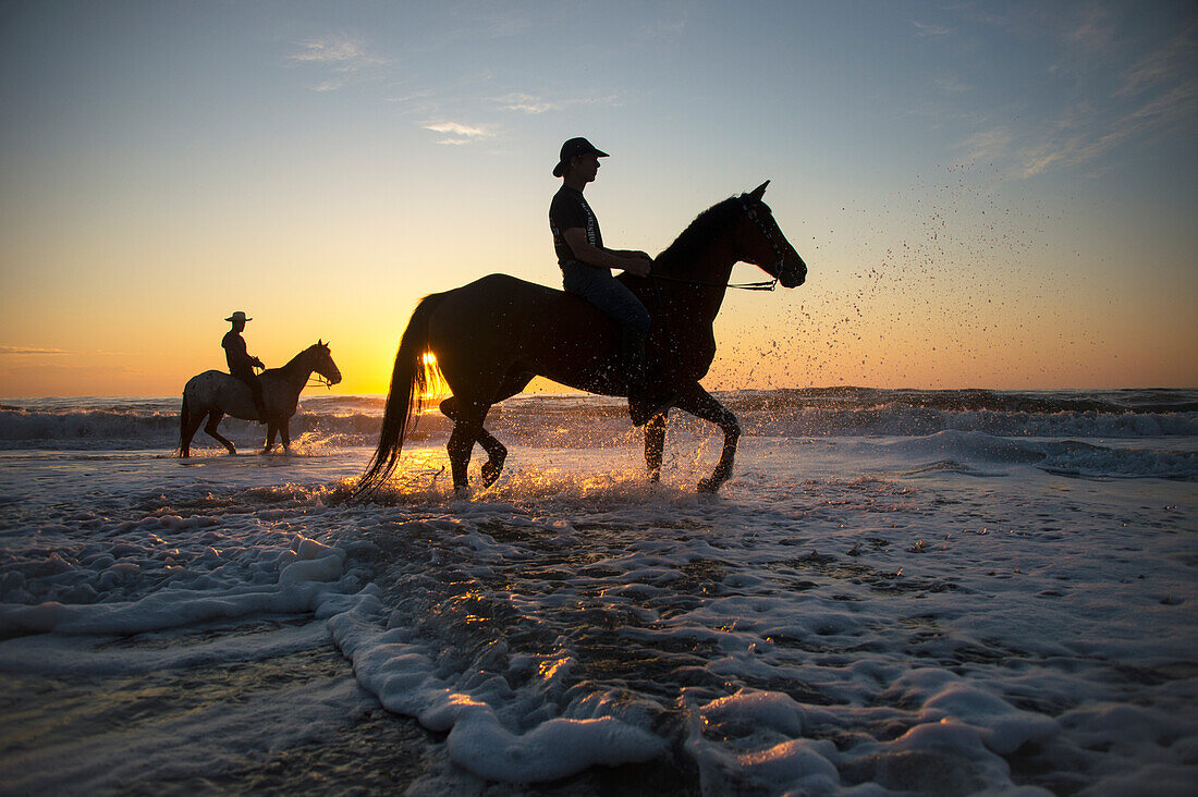 Cowboys reiten auf ihren Pferden bei Sonnenaufgang am Virginia Beach im First Landing State Park,Virginia,USA,Virginia Beach,Virginia,Vereinigte Staaten von Amerika