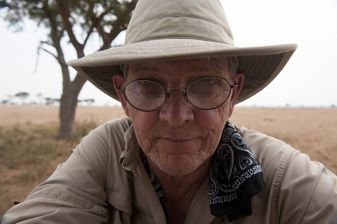 Nahaufnahme eines Mannes im Queen-Elizabeth-Nationalpark, der einen Hut, ein Kopftuch und eine Brille trägt, Uganda