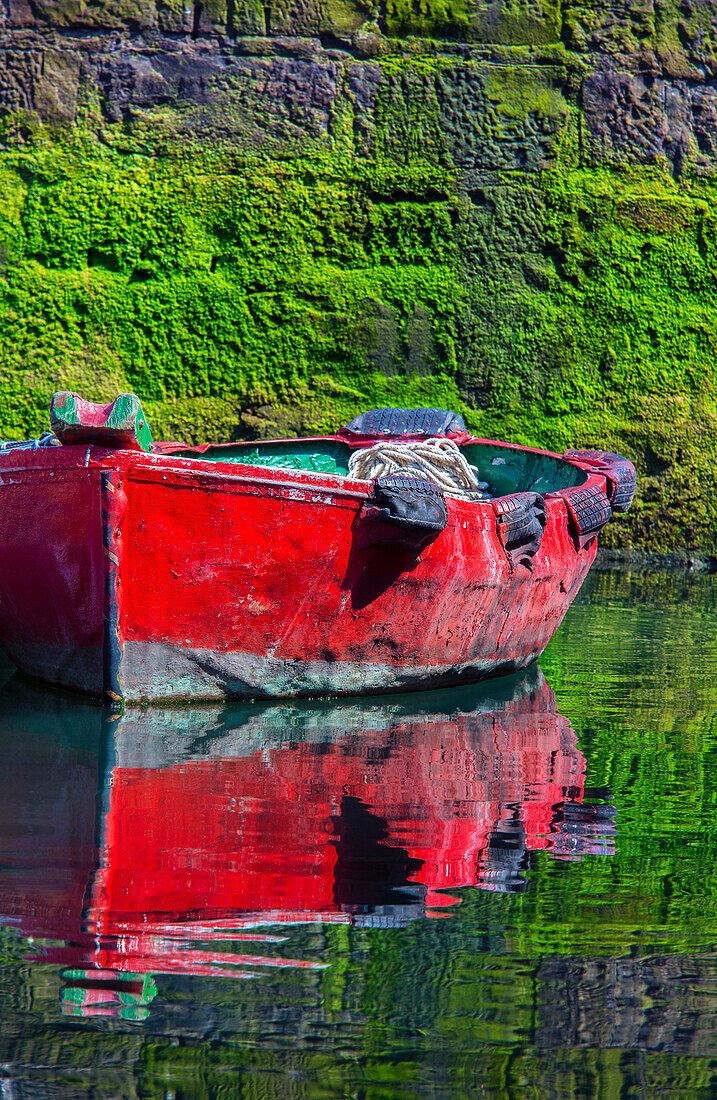 Small,wooden fishing boat moored to the shore with a mirror image reflection in the calm water in the coastal town of Getaria,Getaria,Gipuzkoa,Spain