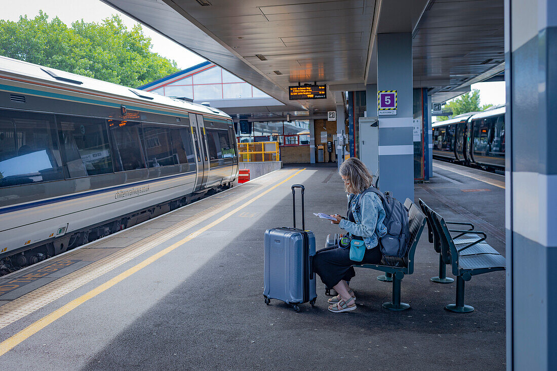 Reife Frau wartet mit Gepäck an einem Bahnhof,Vereinigtes Königreich