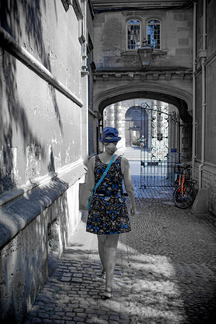 Woman walks down cobblestone alley towards a stone archway in the United Kingdom,United Kingdom