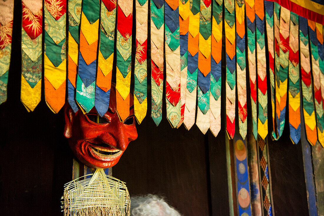 Mask displayed in a farmhouse behind hanging colorful decorative fabric,Paro Valley,Bhutan