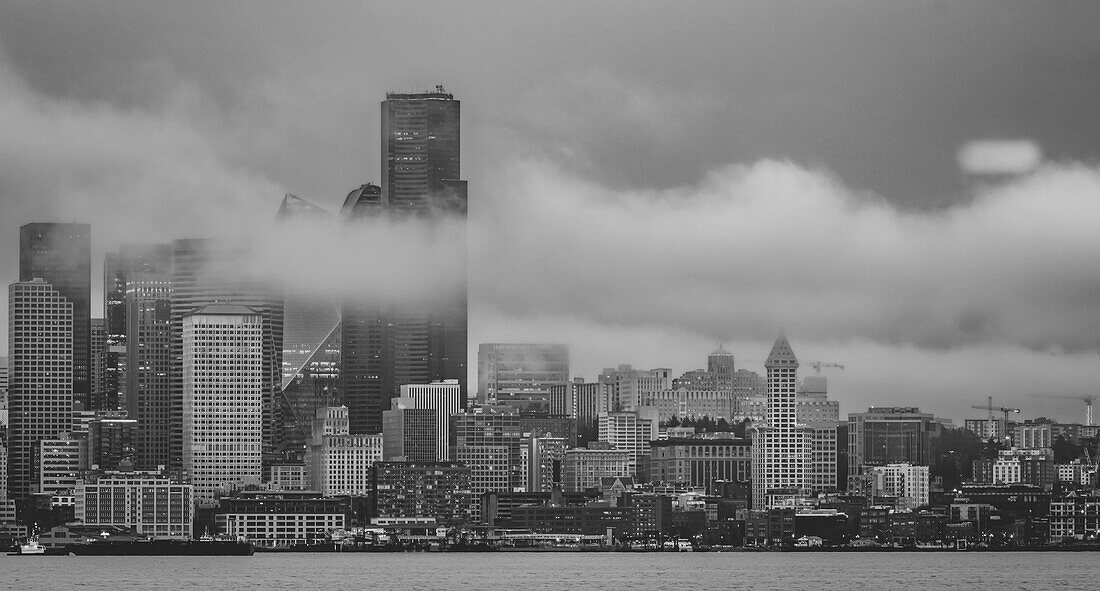 Skyline von Seattle in West Seattle über der Elliott Bay an einem regnerischen Nachmittag mit tief hängenden Wolken und Nebelschwaden, die durch die hohen Gebäude driften, Seattle, Washington, Vereinigte Staaten von Amerika