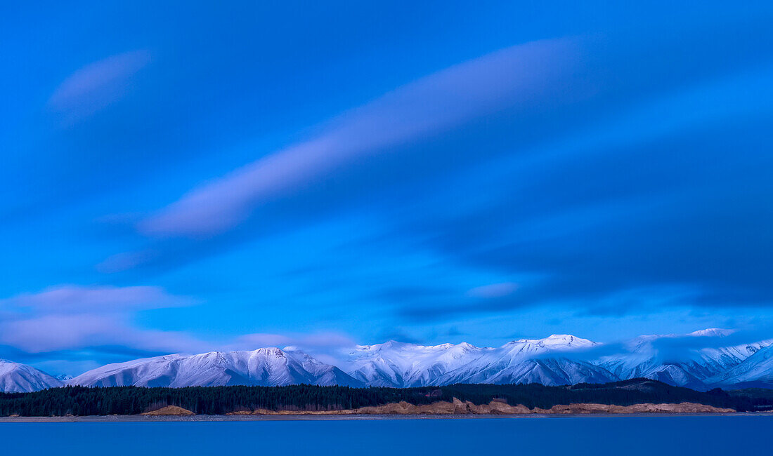 Fresh snow blankets Rhoboro Hills at sunrise with a tranquil Lake Pukaki in the foreground,Twizel,South Island,New Zealand