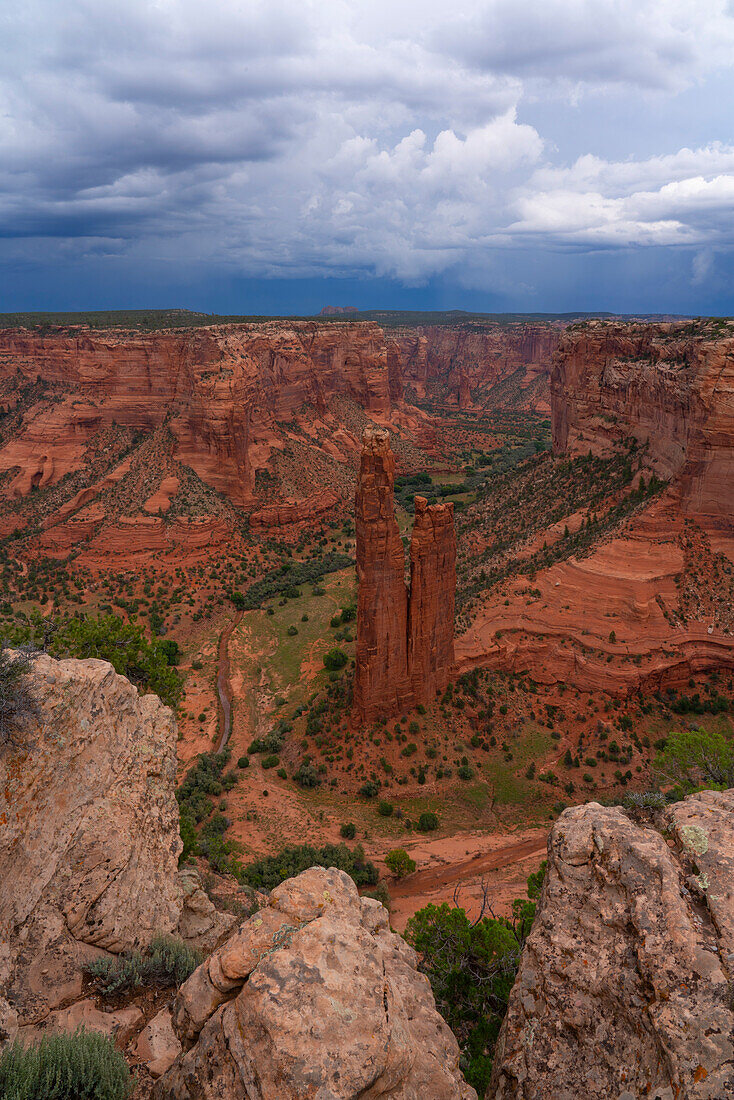 Overview of the Canyon de Chelly with the rock formation known as Spider Rises emerging from the canyon,valley floor surrounded by the eroded red rock landscape under a stormy sky,Arizona,United States of America