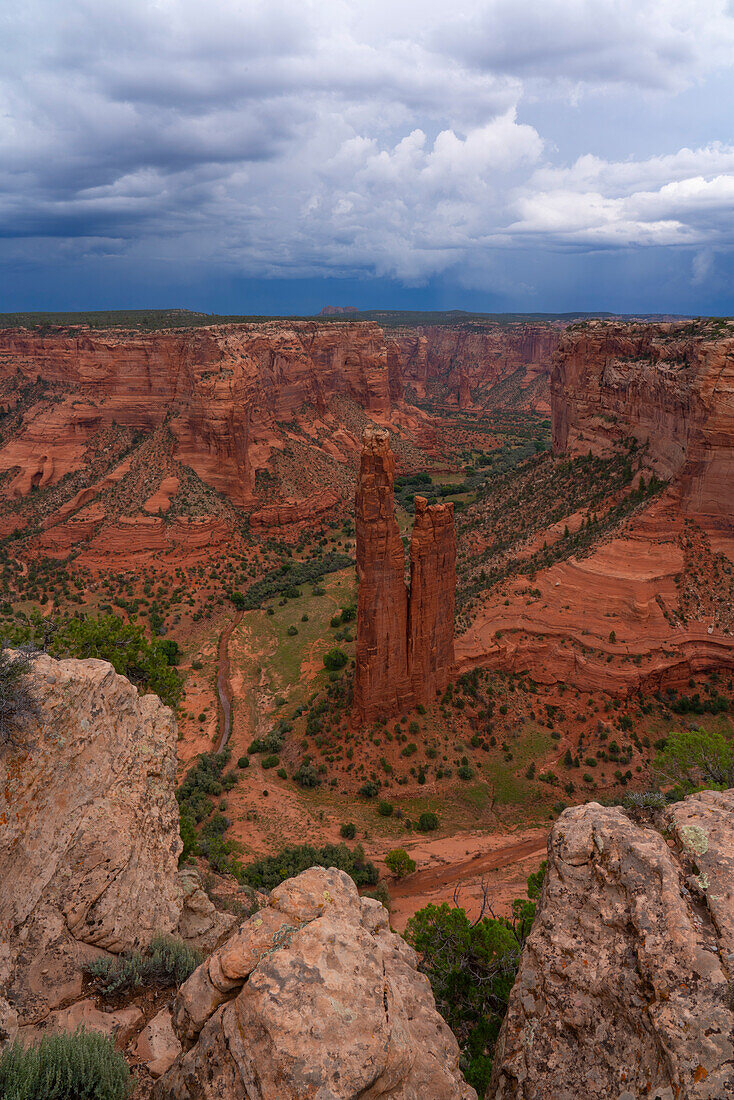 Überblick über den Canyon de Chelly mit der als "Spider Rises" bekannten Felsformation, die sich aus dem Canyon erhebt, Talboden, umgeben von der erodierten roten Felslandschaft unter einem stürmischen Himmel, Arizona, Vereinigte Staaten von Amerika