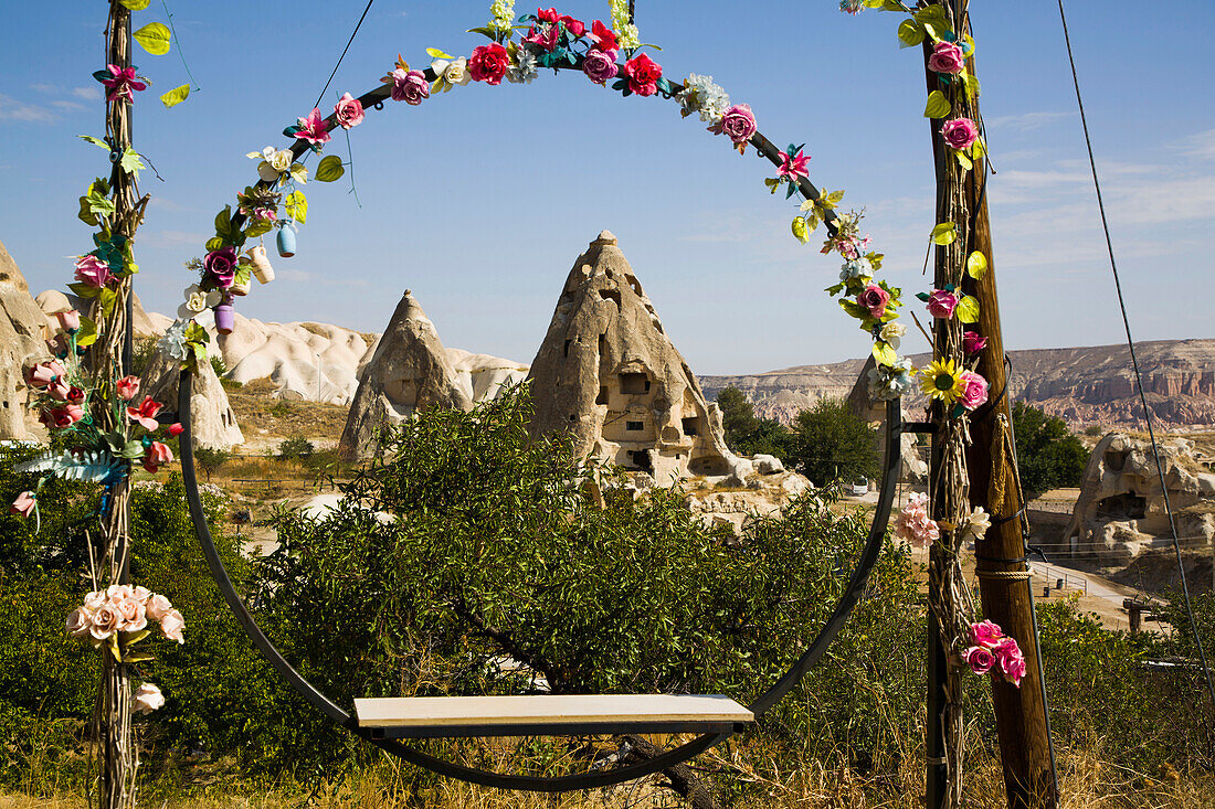 View through a circular swing seat decorated with silk flowers,of the Cave Houses carved into the rock formations against a blue sky near the town of Goreme in Pigeon Valley,Cappadocia Region,Nevsehir Province,Turkey