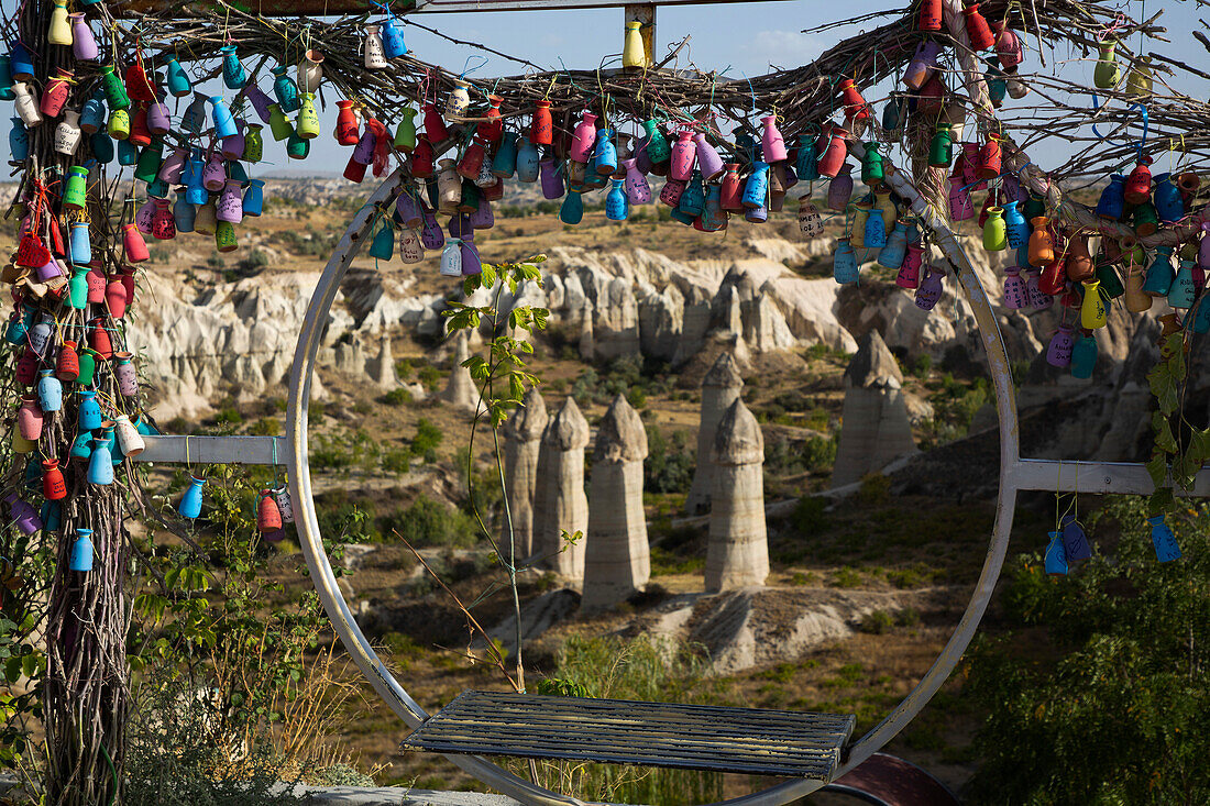 Blick durch einen kreisförmigen Schaukelsitz, der mit bunt bemalten Keramikvasen verziert ist, auf die Feenkamin-Felsformationen im Liebestal nahe der Stadt Goreme, Region Kappadokien, Provinz Nevsehir, Türkei