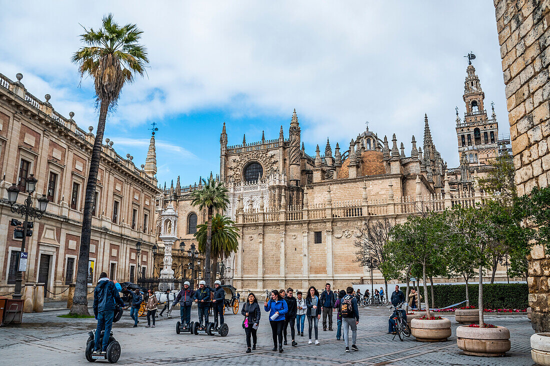 Segways und Touristen auf der Plaza del Triunfo, mit der Kathedrale von Sevilla rechts und dem Generalarchiv der Indios links, Sevilla, Spanien