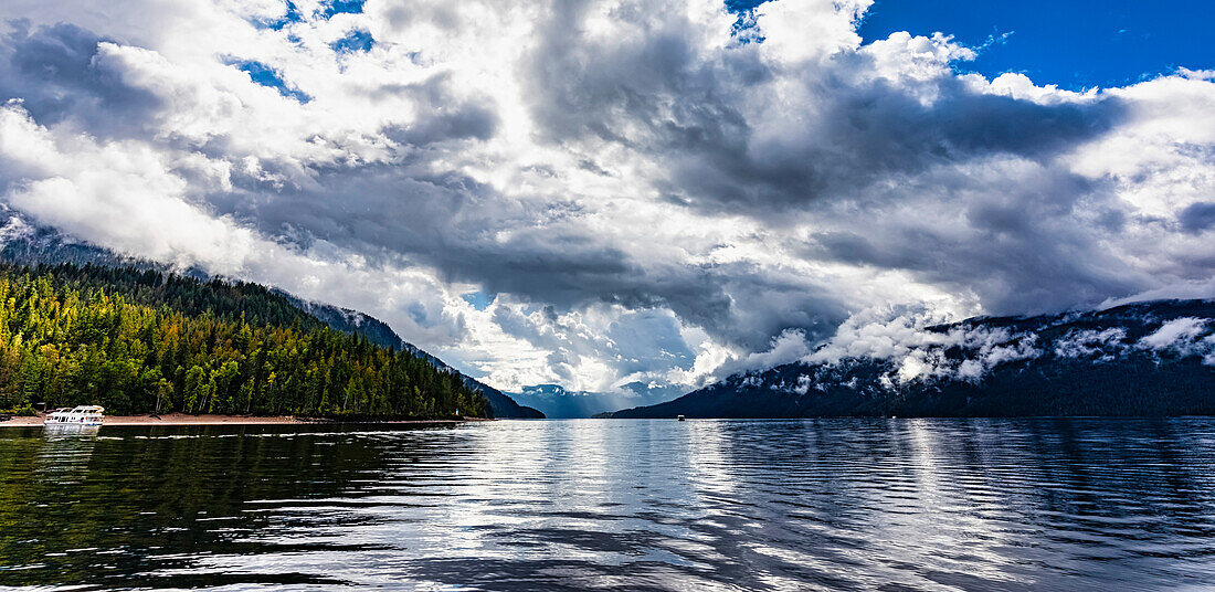 Scenic view of beautiful Shuswap Lake with dramatic clouds in the sky and a houseboat moored to the shore and a boat out on the water during the autumn season,Shuswap Lake,British Columbia,Canada