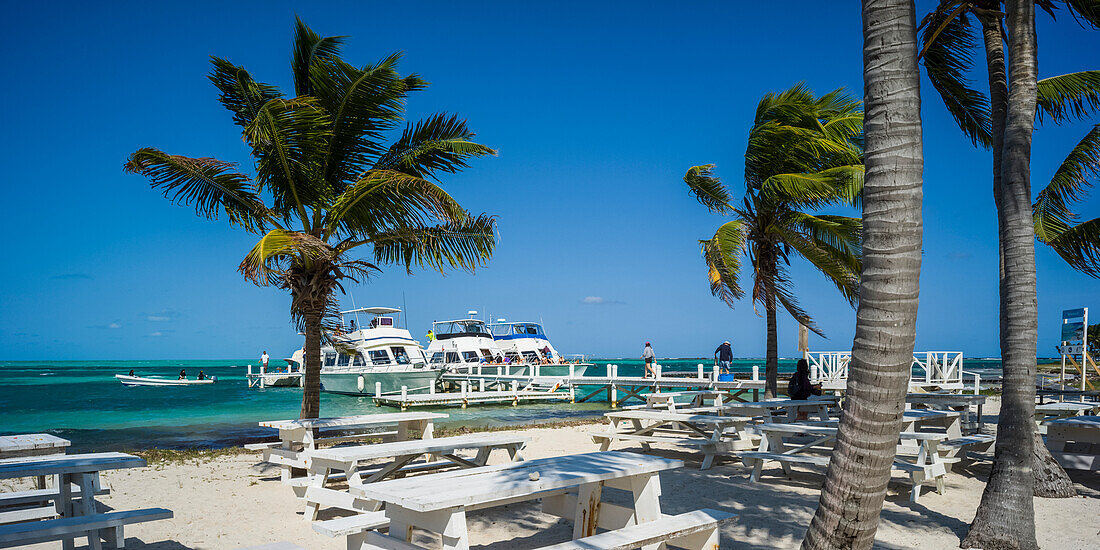 White sand beach with picnic tables and moored boats in the Caribbean,Belize