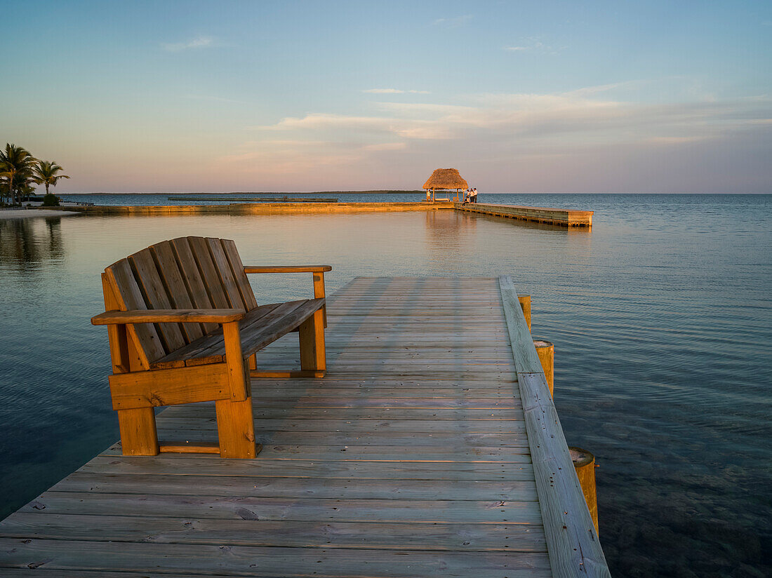 Eine Holzbank auf einem Dock und offener Ozean bei Sonnenuntergang, Belize