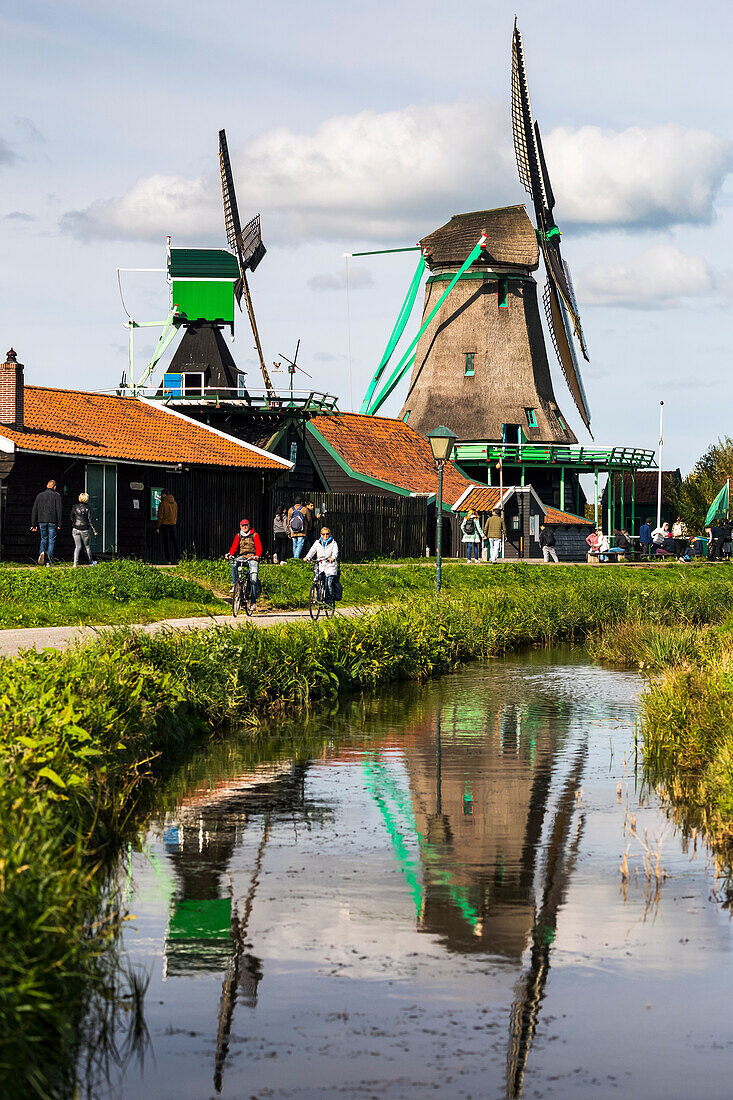 Historical wooden windmills reflecting in small canal with bike path and cyclists,Zaandam,Netherlands