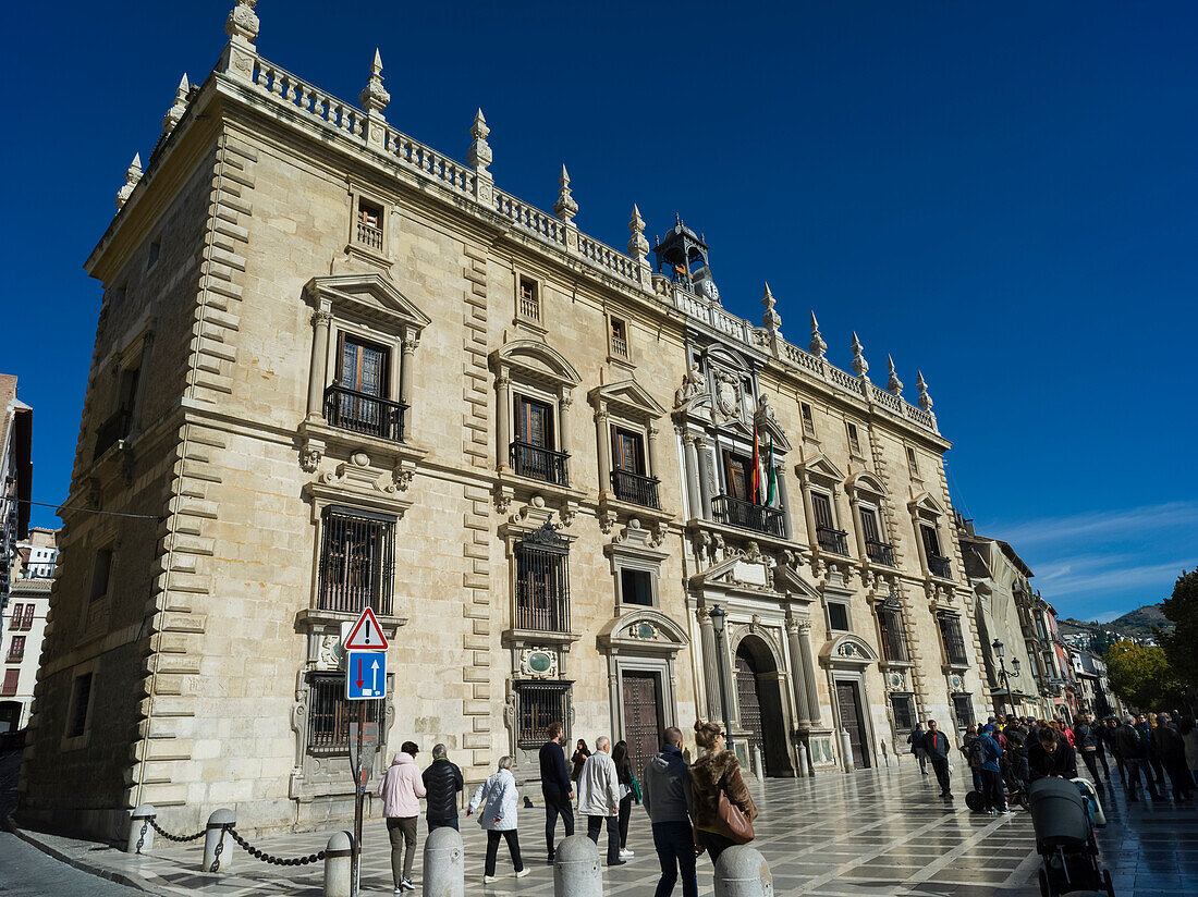 Pedestrians walking past a building in Plaza Neuva with bright blue sky,Granada,Andalusia,Spain