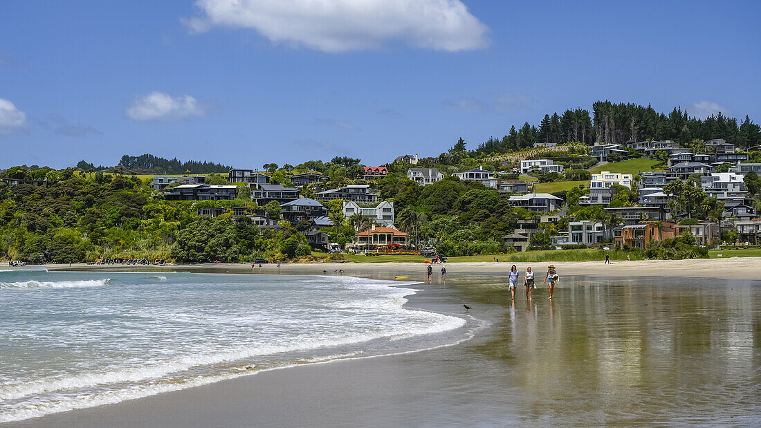 Menschen spazieren entlang der Brandung auf dem nassen Sand von Langs Beach, North Island, Waipu, Northland Region, Neuseeland