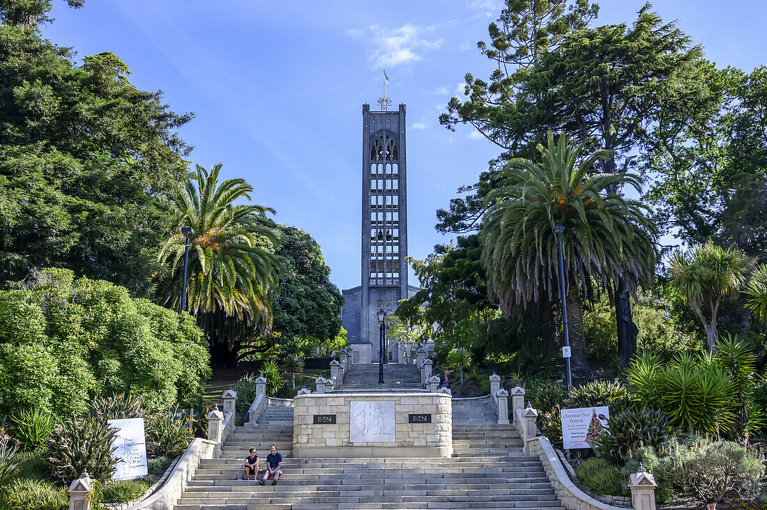 People sitting on the Cawthron Steps with the imposing concrete tower,leading to the Christ Church Cathedral on Church Hill in Nelson,South Island,New Zealand