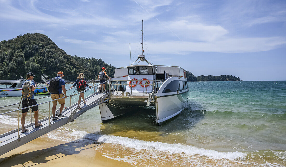 Touristen gehen über eine Rampe, um ein Ausflugsboot im Abel Tasman National Park zu besteigen, einem Wildnisgebiet am nördlichen Ende der Südinsel Neuseelands, Tasman District, Neuseeland