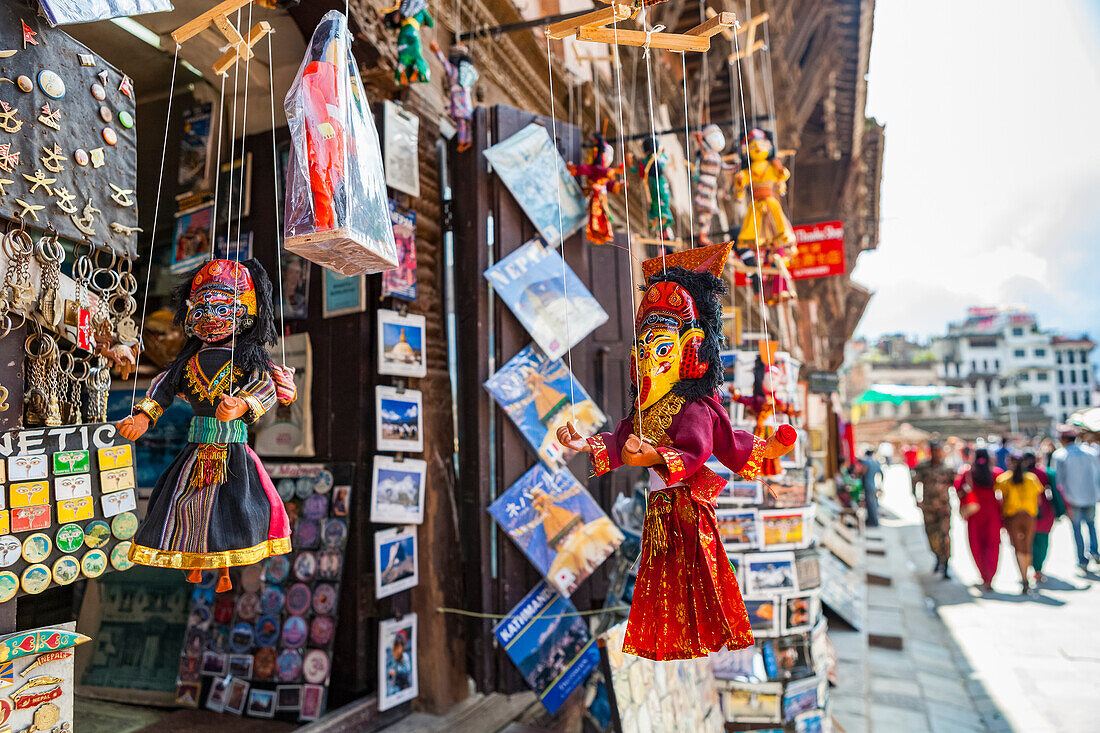 Touristen spazieren an Marionetten, Magneten, Postkarten und anderen Souvenirs vorbei, die in Souvenirläden außerhalb des Durbar Square verkauft werden, an einem sonnigen, aber smogigen Tag in Kathmandu, Nepal, Kathmandu, Nepal