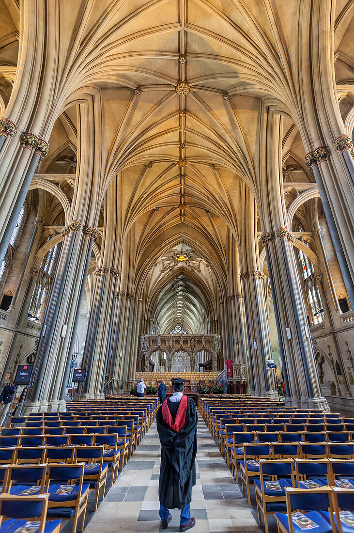 Student (graduand),wearing traditional robe and mortar board,watching preparations for the university graduation ceremony in Bristol Cathedral,Bristol,South West England