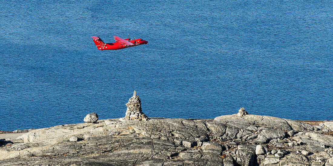 Kleines rotes Flugzeug fliegt über die zerklüftete, felsige Küste Grönlands, Nuuk, Sermersooq, Grönland