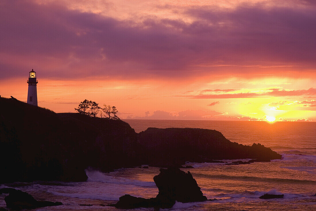 Yaquina Head Light bei Sonnenuntergang, mit einem glühenden rosa Himmel und heller Sonne, die entlang der Küste von Oregon im Pazifik versinkt,Oregon,Vereinigte Staaten von Amerika