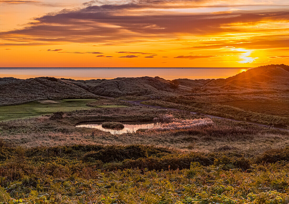 Sonnenaufgang über der Nordsee und dem Golfplatz an der Küste im Dorf Warkworth, Northumberland, England, Vereinigtes Königreich